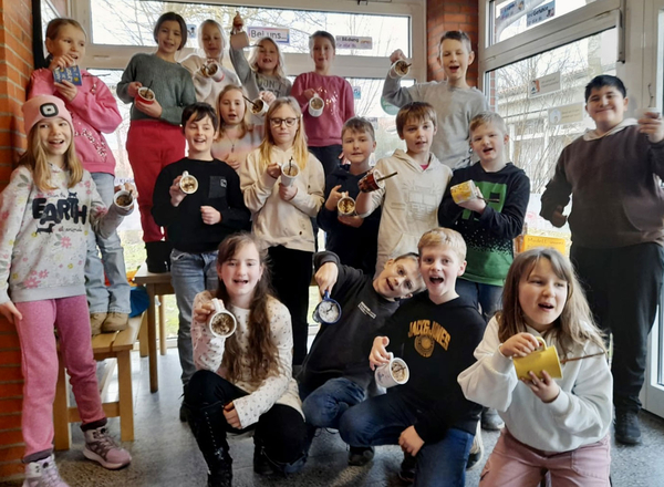 Schulklasse 3b der Reimer-Bull-Schule in Marne hält die selbstgebastelten Vogelfutter hoch, die Kinder lächeln und freuen sich!